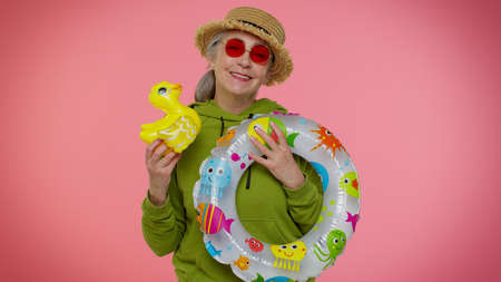 Cheerful senior old granny woman traveler tourist dancing fooling with swimming ring and inflatable...