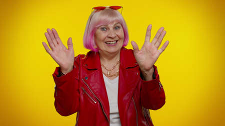 Happy friendly elderly granny woman waves hand palm in hello gesture welcomes someone with...