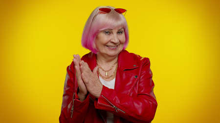Sneaky cunning mature granny woman with tricky face gesticulating and scheming evil plan, thinking over devious villain idea, cunning cheats, jokes and pranks. Senior grandmother on yellow backgroundの写真素材