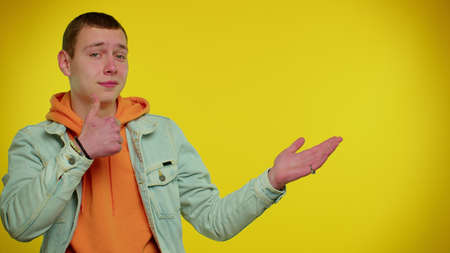 Handsome stylish teen boy showing thumbs up and pointing empty place, advertising area for...