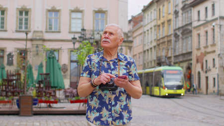 Elderly stylish tourist man looking for way using smartphone in old town Lviv, Ukraine. Senior mature traveler guy grandfather pensioner getting lost in big city trying to find route. Summer vacationの写真素材