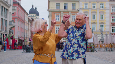 Elderly stylish couple tourists man woman celebrate success win scream rejoices doing winner hands gesture say Yes. Senior travelers grandmother, grandfather enjoying time together. Summer vacationの写真素材