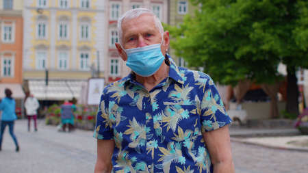 portrait of senior stylish tourist man grandfather wearing protective mask on city street crowd people.の写真素材