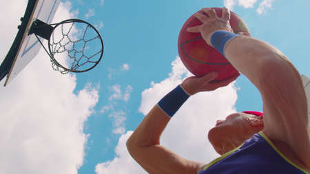 Upward view of focused senior player man playing basketball game, successfully hits goal. Active...