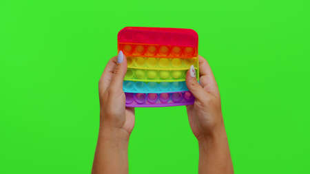 Close-up of girl hands playing squeezing anti-stress toys pop up game isolated on chroma key. Popular educational simple dimple touch screen game with buttons. Autism Special Needs Stress Relieverの写真素材