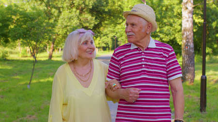 Senior old stylish tourists man and woman having a walk and talking in summer park. Elderly grandmother, grandfather enjoying conversation, traveling together. Active mature family after retirementの写真素材