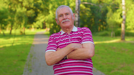 Happy stylish senior old gray-haired man in casual red t-shirt posing isolated on summer park...
