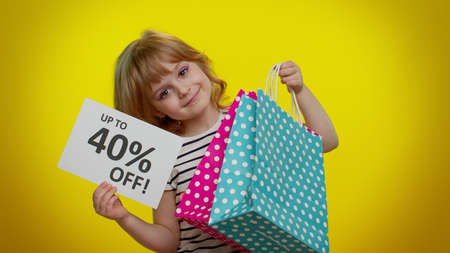 Little blonde teen kid child girl showing shopping bags and Up To 40 Percent Off inscriptions banner text. Black Friday. Good holiday discounts, low prices for shopping. Children on yellow backgroundの写真素材