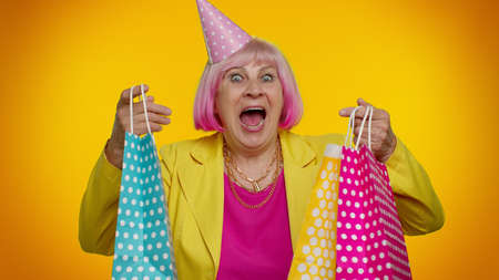 Elderly granny stylish woman showing shopping bags, advertising discounts, smiling looking amazed...