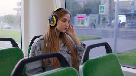 Young woman wearing headphones listening music, funny relax dancing while traveling by bus to city...