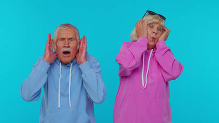 Stressed depressed elderly woman granny with man grandfather expresses their fear and waves hands away from danger, waving no isolated on blue studio background. Senior grandmother with grandpaの写真素材