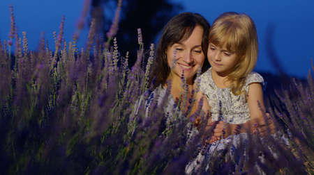 Happy young mother and little girl daughter kid kissing and laughing in aromatic flowers lavender field garden on summer night sunset. Family, childhood, motherhood, fairytale, provence style conceptの写真素材