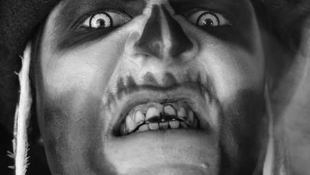 Close-up shot of creepy man face with skeleton makeup. Guy making faces, trying to scare, opening his mouth, showing dirty black teeth. Voodoo rituals. Halloween demon party. Black and white portraitの写真素材
