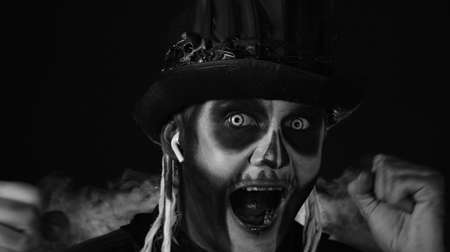 Creepy man with skeleton makeup in top-hat with feathers. Guy wearing earphones, listening music,...