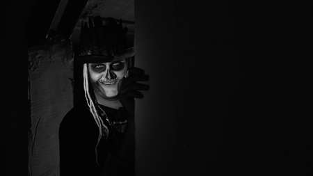 Creepy man with horrible Halloween skeleton makeup in costume with top-hat slowly appears from dark...