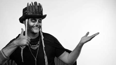 Sinister man with horrible Halloween skeleton makeup in costume with top-hat looking at camera,...