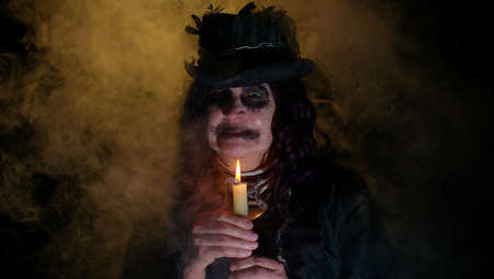 Portrait of sinister senior old mature woman in carnival costume of Halloween witch. Voodoo magic rituals with candle isolated on black studio background. Horror theme of cosplay clown, vampire, beastの写真素材