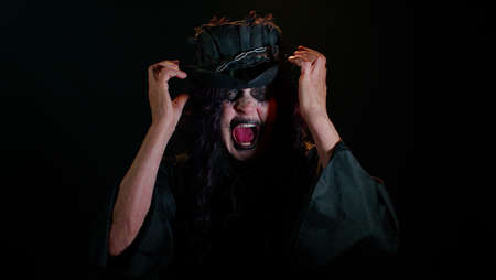 Sinister old woman in costume of Halloween witch screams from stress tension problems feels horror hopelessness fear surprise shock expresses gestures rage. Horror theme of cosplay clown vampire beastの写真素材
