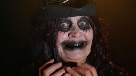 Portrait of sinister senior old mature woman in carnival costume of Halloween witch making faces,...