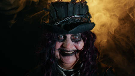 Creepy mature woman grandmother with Halloween stylish witch makeup. Old scary granny making faces, looks at camera and smiles terribly. Voodoo rituals. Thematic party. Sinister senior lady vampireの写真素材