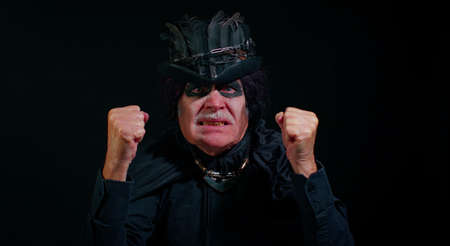 Frustrated sinister man with horrible scary Halloween witcher makeup raising hands in indignant expression, quarreling, asking reason of conflict why such stubborn. Vampire grandpa on black backgroundの写真素材