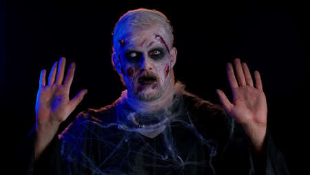 Surrender. Sinister man in costume of Halloween crazy zombie with bloody wounded scars face scared...