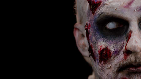 Close-up face of sinister man with horrible scary Halloween zombie makeup making faces, looking ominous at camera, trying to scare. Dead guy with wounded bloody scars face isolated on black backgroundの写真素材