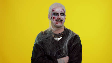 Cheerful happy creepy man with bloody scars face, Halloween stylish zombie make-up. Scary wounded undead guy making faces, looks at camera and smiles terribly with dirty teeth. Sinister beast, monsterの写真素材