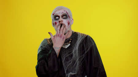 Oh my God, Wow. Scary man with Halloween zombie bloody wounded makeup raising hands in surprise looking at camera with big eyes, shocked by sudden victory. Excited amazed sinister undead guy aloneの写真素材