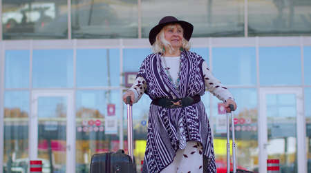 Senior pensioner tourist grandmother business woman walking away from international airport hall or railway station while carrying luggage suitcase on wheels. Travel, vacation, journey, trip, holidaysの写真素材