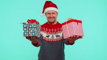Portrait of fun adult man wears red New Year presenting Christmas gift boxes, stretches out his...