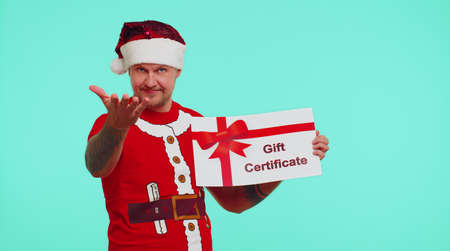 Funny 30s years old man wears red New Year t-shirt and hat presenting card gift certificate coupon...