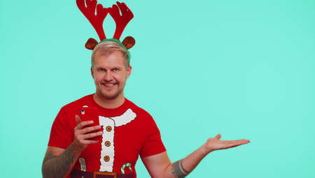 Man in t-shirt Santa Christmas with mobile phone showing pointing empty place, advertising area for...