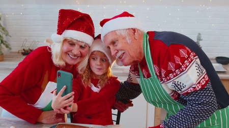 Smiling mature grandparents couple with granddaughter taking selfie photo on mobile phone at...