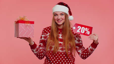 Happy girl in red New Year sweater showing gift box and 20 Percent discount inscriptions banner...