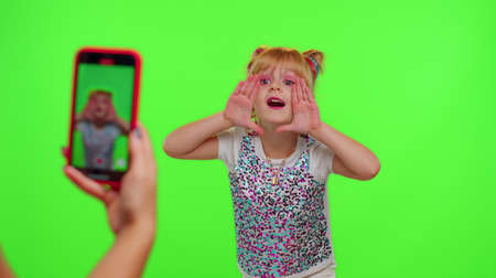 Lovely little Caucasian kid girl blogger front of phone camera record video enjoy dance content on green chroma key background. Social distance virus pandemic concept. Freedom active lifestyleの写真素材