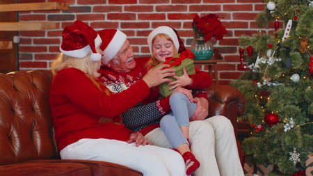 Grandfather, grandmother gifting Christmas present box to amazed happy grandchild girl kid at home....