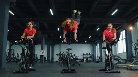 Class group of young women exercising on stationary cycle machine bike in gym. Modern sport...