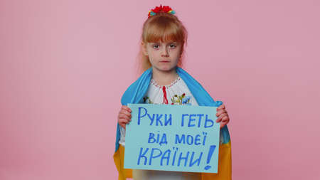Ukrainian translation: Hands Off From My Country. Little kid toddler girl in embroidery dress holding banner with inscription massage text, protesting war conflict. Crisis, no peace, stop aggressionの写真素材