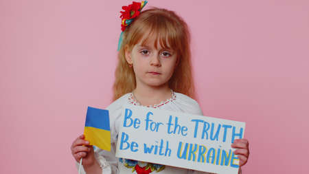 Sad toddler Ukrainian girl kid in embroidery dress protesting war conflict raises national flag and banner with inscription Be For The Truth Be With Ukraine. Peace, no war, stop russian aggressionの写真素材