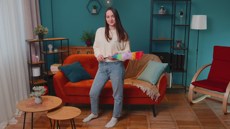 Happy one young woman dusting cleaning furniture caring for hygiene using colorful duster in living...