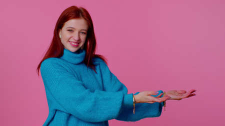 Pretty redhead teen girl showing thumbs up and pointing empty place, advertising area for commercial...