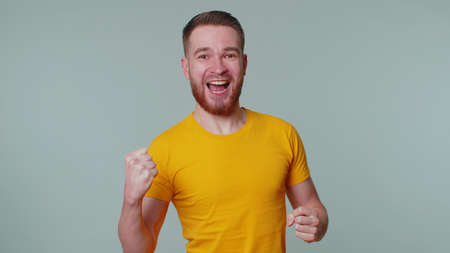 Handsome stylish man in casual yellow t-shirt shouting, raising fists in gesture I did it,...