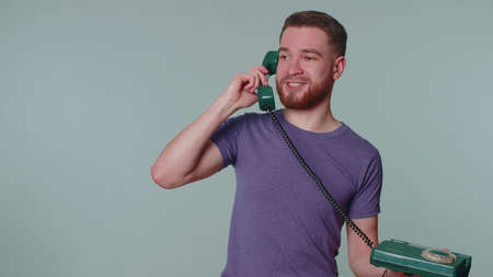 Hey you, call me back. Cheerful man secretary in purple t-shirt talking on wired vintage telephone...
