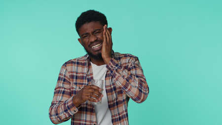 African american man drinking water touching sore cheek suffering from toothache cavities or...