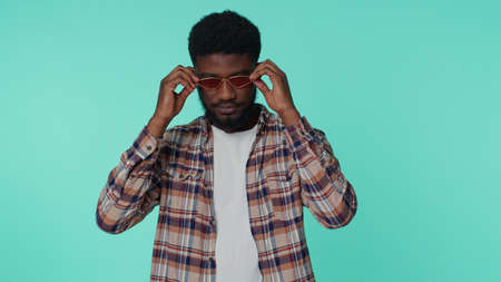 Portrait of one candid cheerful stylish african american man wearing sunglasses, charming smile. People emotions concept. Young lovely adult guy posing isolated alone on blue studio wall backgroundの写真素材