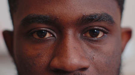 Close-up macro portrait of natural beauty young beautiful african american mans eyes, looking at camera. Brown eyes of man face, guy male model. Boy opening blinking his eyes. Slow motion 4k footageの写真素材