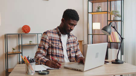African american man freelancer using laptop computer sitting at desk working from home office. Guy...