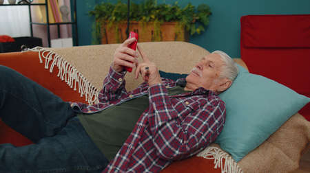 Smiling Caucasian senior grandfather use mobile cell phone, receive good news message, found out...