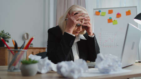 Tired senior mature older business woman use laptop, having nervous breakdown at work, migaine, headache, stress management, mental distress problems, losing temper, reaction on failure at home officeの写真素材